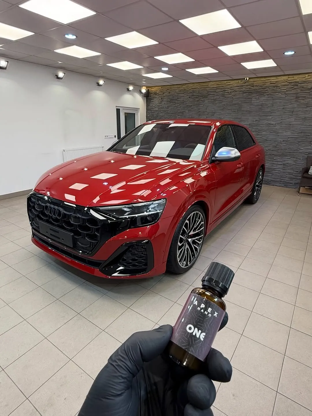 Fľaštička nano ochrany Titan Coatings v ruke detailera pred ošetreným vozidlom v štúdiu UMYSI